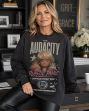 Load image into Gallery viewer, A woman wearing a dark charcoal graphic sweatshirt with a vintage-style print of a doll and the text 'THE AUDACITY PLASTIC PANIC UNAPOLOGETICALLY BOLD!' and 'WWW.AUDACITYSIGNS.
