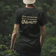 Load image into Gallery viewer, Woman with cap on backwards walking away wearing the &quot;Transformation Never Diminishes Beauty&quot; Black T-Shirt, in a forrest. 
